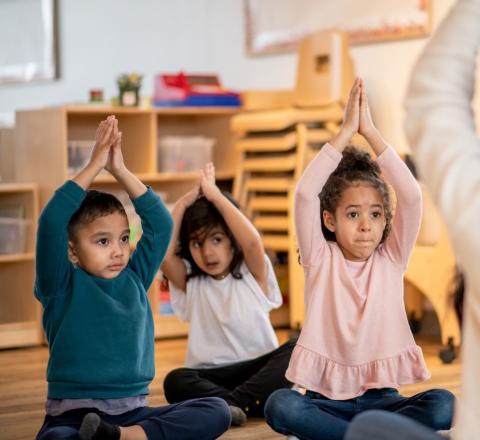 children seated with hands clasped overhead