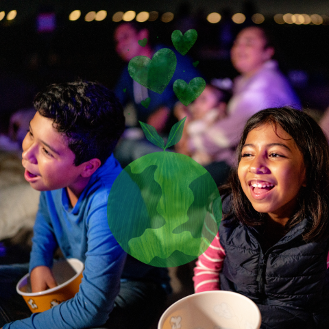 Two smiling children watching a movie. A green planet earth and hearts is superimposed over the image.