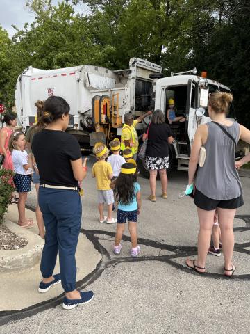 Children and adults standing next to a garbage truck.
