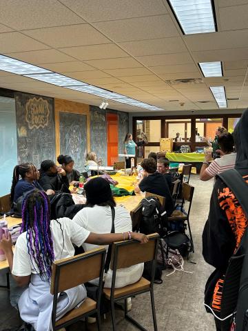 Teenagers sit around a table while a wildlife educator at the front of the room holds a hawk