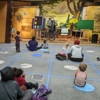 Ms. Sharon in Story Time with children and adults sitting on the floor