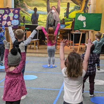 Ms. Sharon in Story Time with children stretching their hands up