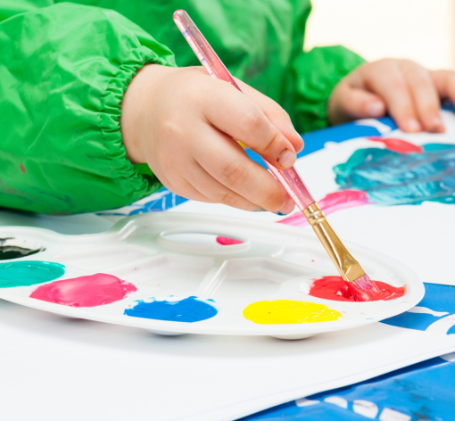 Child's hand holding paintbrush with paint palette