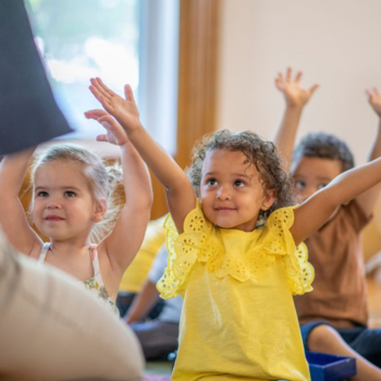 Smiling children stretching their arms overhead during story time.