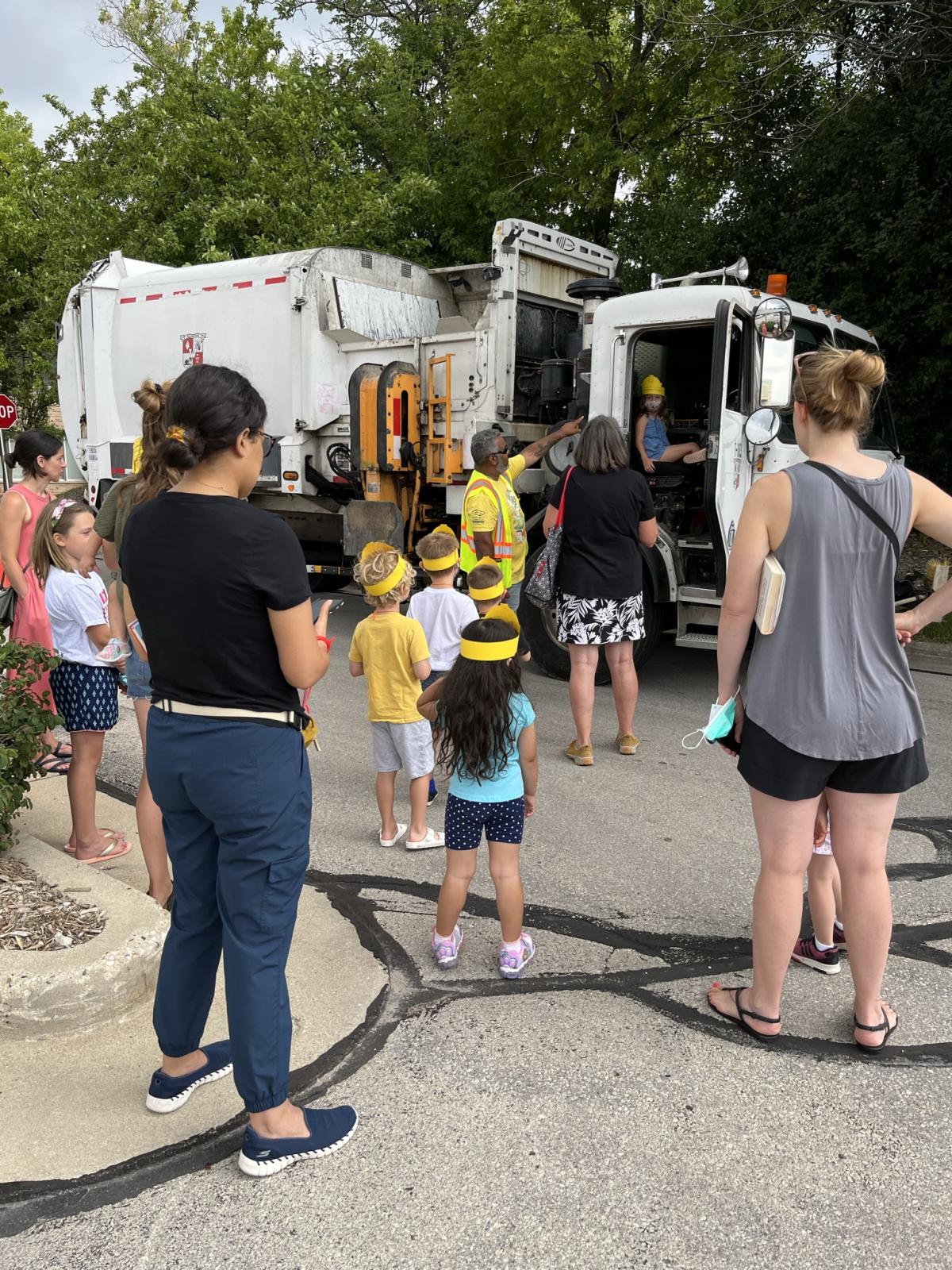 Children and adults standing next to a garbage truck.
